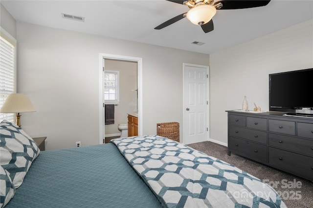 bedroom with dark colored carpet, baseboards, visible vents, and ensuite bath