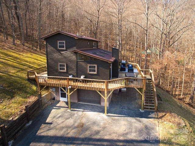 rustic home featuring driveway, an attached garage, stairway, and a wooden deck