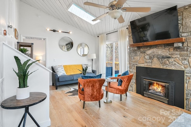 living area with light wood-type flooring, wooden ceiling, vaulted ceiling with skylight, and a stone fireplace