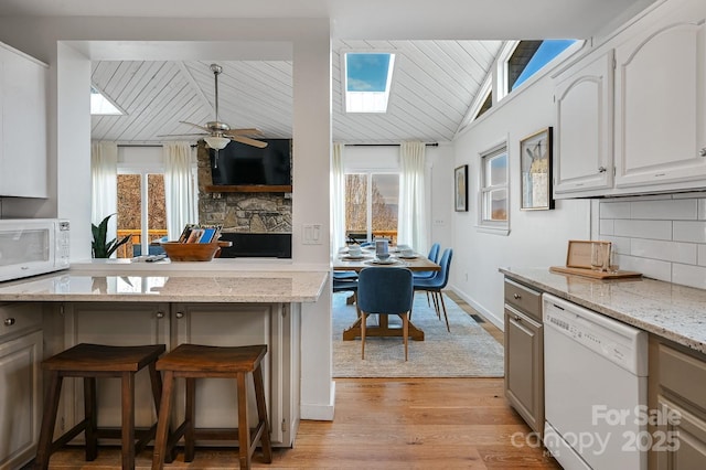 kitchen featuring a breakfast bar, backsplash, light wood-type flooring, vaulted ceiling with skylight, and white appliances