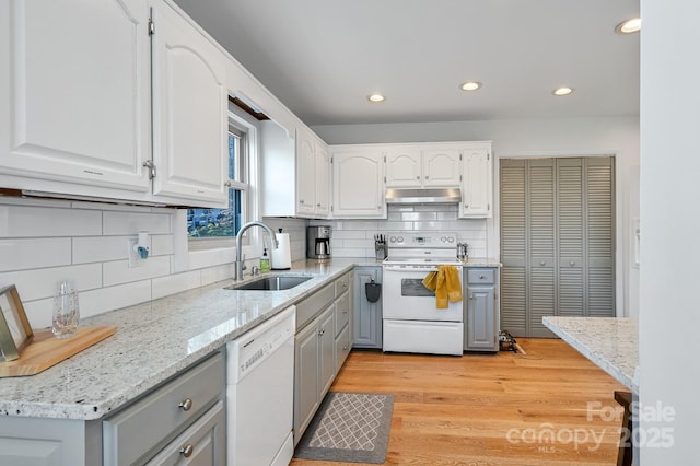 kitchen featuring under cabinet range hood, white appliances, a sink, white cabinetry, and light wood-style floors