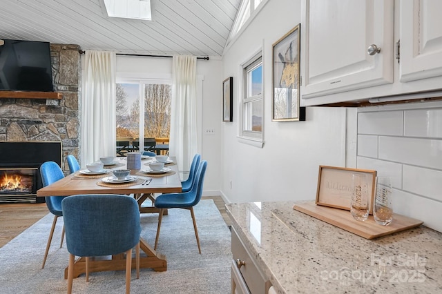 dining space featuring light wood-type flooring, wooden ceiling, and a stone fireplace