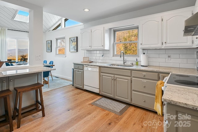 kitchen with tasteful backsplash, lofted ceiling, range hood, white dishwasher, and a sink