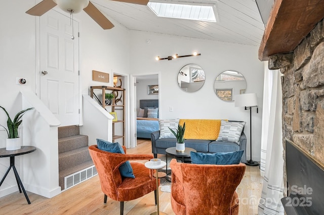 sitting room with light wood finished floors, vaulted ceiling with skylight, stairway, and visible vents