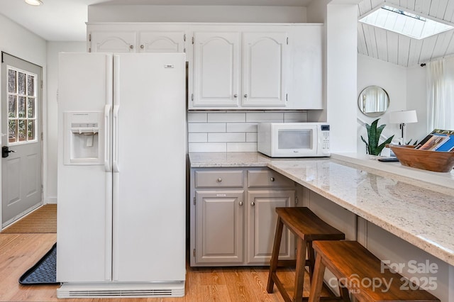 kitchen with light stone counters, white appliances, light wood-style floors, white cabinets, and backsplash