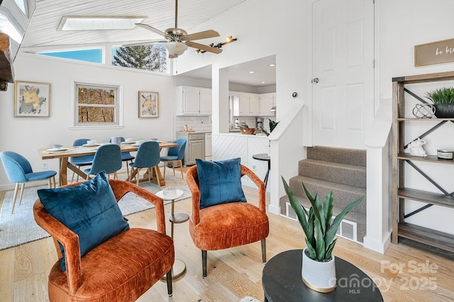 sitting room with ceiling fan, high vaulted ceiling, baseboards, stairs, and light wood-style floors