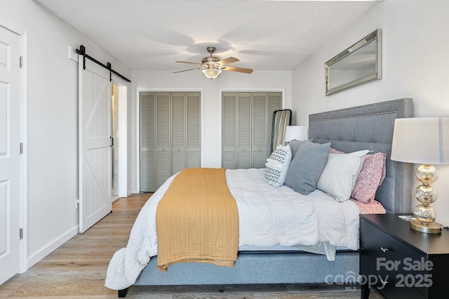 bedroom with a textured ceiling, a barn door, a ceiling fan, light wood-style floors, and multiple closets