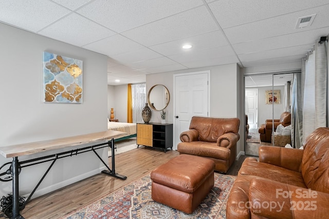 living area featuring a paneled ceiling, visible vents, baseboards, and wood finished floors