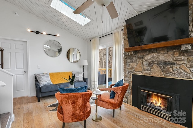 living area with ceiling fan, wooden ceiling, light wood-style flooring, a fireplace, and lofted ceiling with skylight