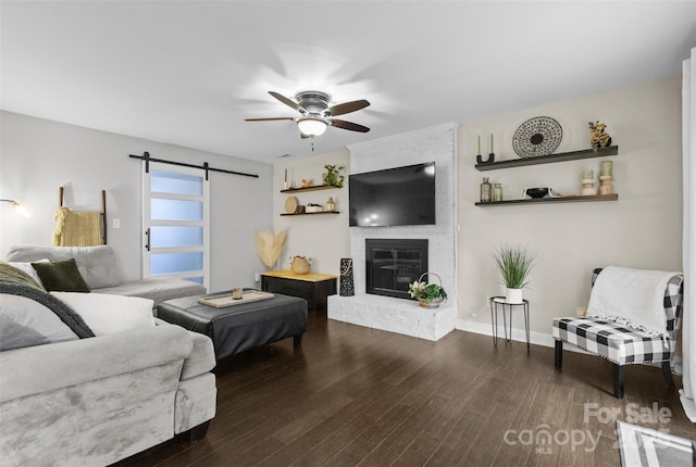 living room with a barn door, wood finished floors, a ceiling fan, baseboards, and a brick fireplace