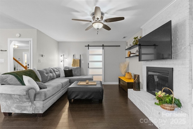 living area with ceiling fan, a barn door, a fireplace, and wood finished floors