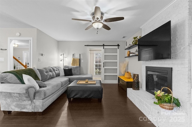 living room with a brick fireplace, wood finished floors, ceiling fan, and a barn door