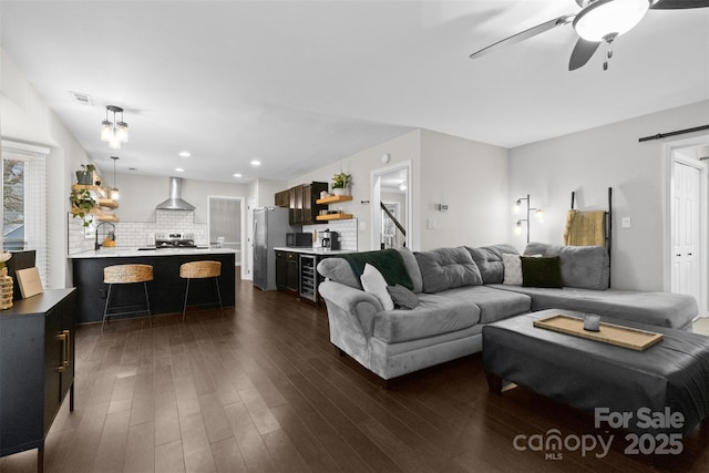 living area featuring a barn door, ceiling fan, wine cooler, dark wood-type flooring, and stairs