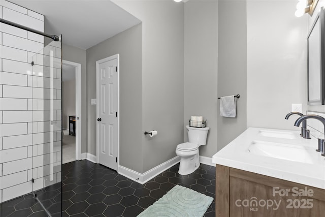 bathroom featuring tile patterned flooring, toilet, vanity, baseboards, and a tile shower