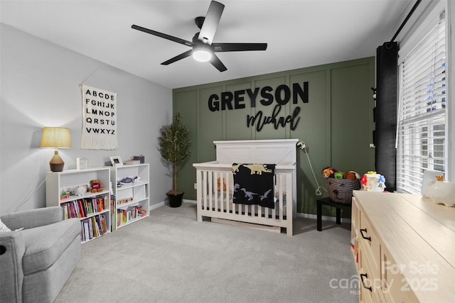 carpeted bedroom with a ceiling fan, a decorative wall, and a crib