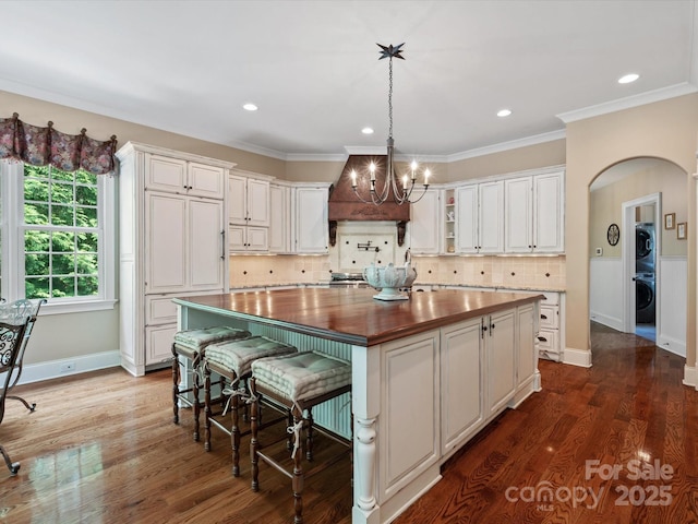 kitchen featuring arched walkways, a kitchen island, wood counters, custom exhaust hood, and white cabinetry