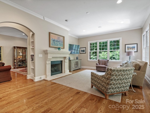 living room with arched walkways, a fireplace with raised hearth, ornamental molding, and wood finished floors