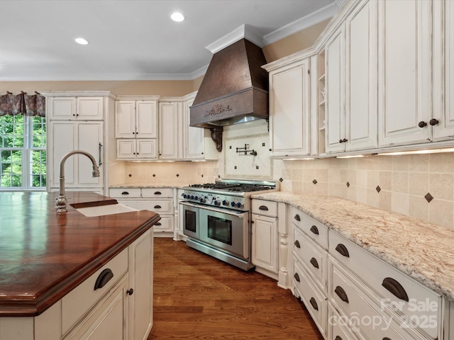 kitchen featuring light stone counters, custom range hood, ornamental molding, white cabinetry, and double oven range