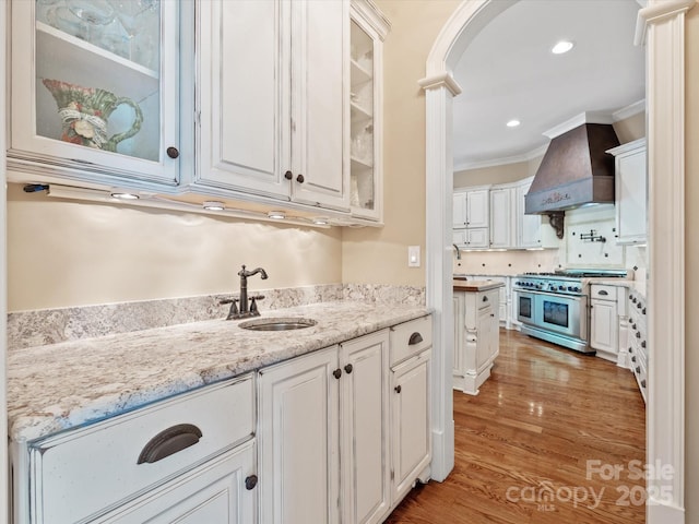 kitchen featuring range with two ovens, premium range hood, a sink, white cabinetry, and glass insert cabinets