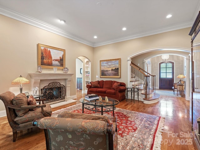 living area with crown molding, a fireplace, arched walkways, and wood finished floors