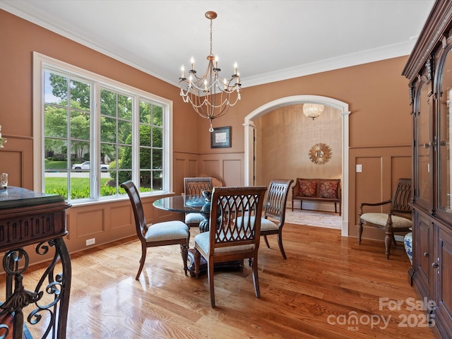 dining area featuring light wood-style floors, arched walkways, crown molding, and a decorative wall