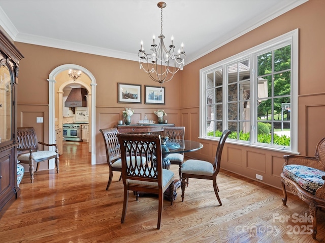 dining area with light wood finished floors, arched walkways, ornamental molding, an inviting chandelier, and a decorative wall