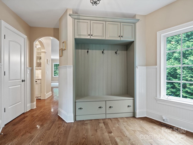 mudroom with arched walkways, a wainscoted wall, visible vents, and wood finished floors