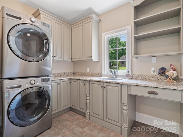 clothes washing area featuring stone finish flooring, stacked washing maching and dryer, a sink, and cabinet space