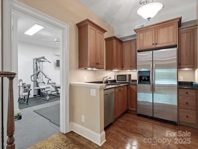 kitchen with visible vents, dark countertops, appliances with stainless steel finishes, brown cabinets, and a sink