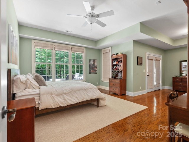 bedroom with ceiling fan, wood finished floors, visible vents, and baseboards