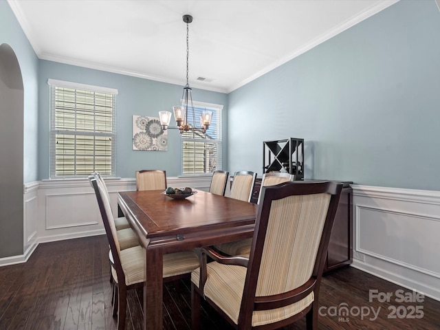 dining area with arched walkways, dark wood-style flooring, a wainscoted wall, and plenty of natural light