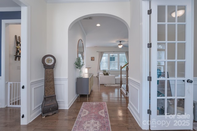 interior space featuring arched walkways, ceiling fan, a decorative wall, dark wood-style flooring, and ornamental molding