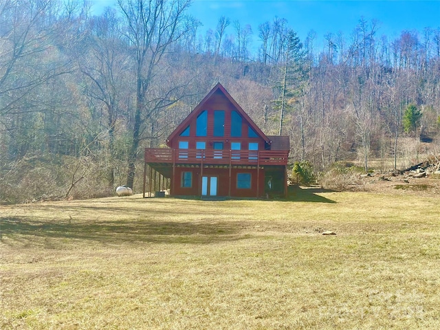 rear view of property with a deck, a view of trees, and a yard