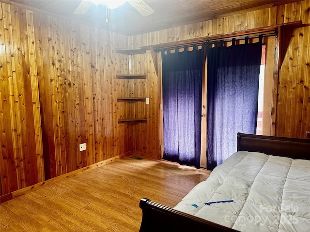 unfurnished bedroom with ceiling fan, wood walls, baseboards, and wood finished floors