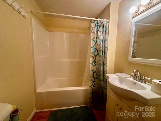 bathroom with a textured wall, vanity, and shower / bath combo with shower curtain