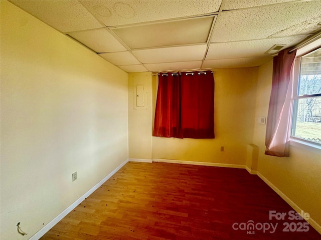 empty room featuring a drop ceiling, wood finished floors, and baseboards