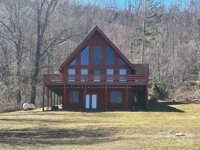 back of property with a wooded view, a deck, and a lawn