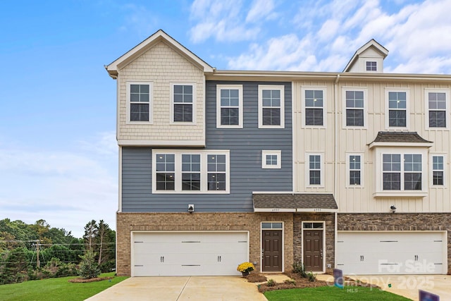 view of property featuring an attached garage, brick siding, driveway, a front lawn, and board and batten siding