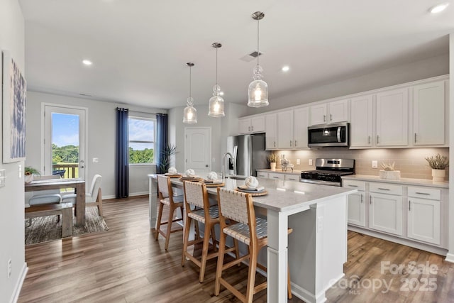kitchen featuring pendant lighting, stainless steel appliances, a center island with sink, and white cabinets