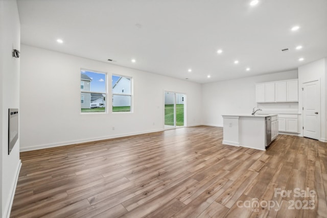 kitchen with open floor plan, a kitchen island with sink, light countertops, light wood-style floors, and white cabinetry