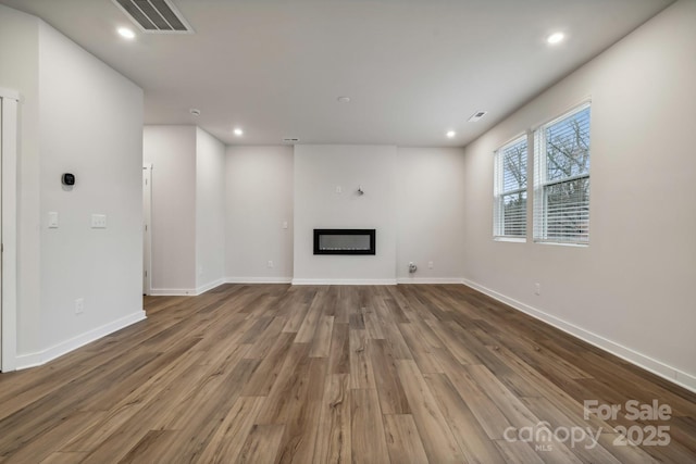 unfurnished living room featuring recessed lighting, wood finished floors, visible vents, baseboards, and a glass covered fireplace