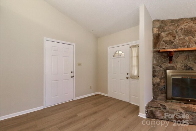 foyer entrance with a textured ceiling, a stone fireplace, wood finished floors, baseboards, and vaulted ceiling