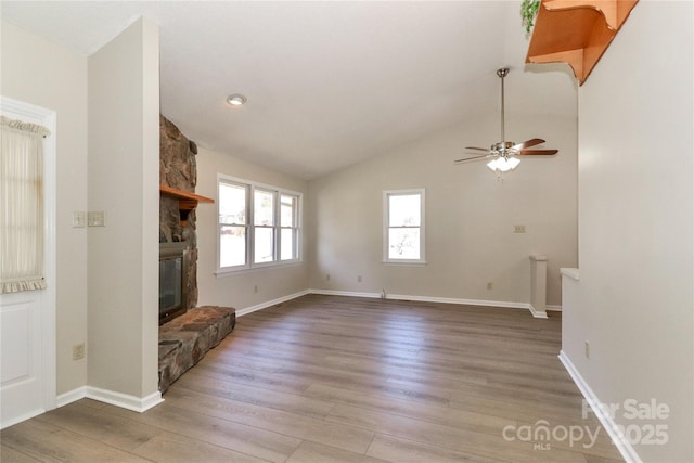 unfurnished living room featuring lofted ceiling, light wood finished floors, ceiling fan, and a stone fireplace