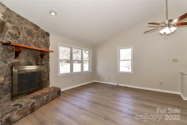 unfurnished living room with baseboards, vaulted ceiling, wood finished floors, and a stone fireplace