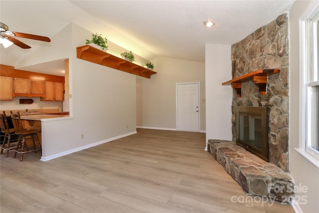 living area with lofted ceiling, a stone fireplace, a ceiling fan, baseboards, and light wood-type flooring