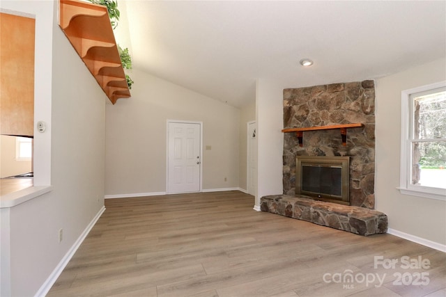 unfurnished living room with baseboards, vaulted ceiling, wood finished floors, and a stone fireplace