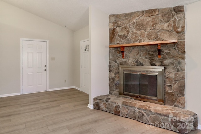 unfurnished living room featuring lofted ceiling, a fireplace, baseboards, and wood finished floors