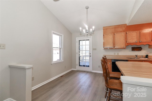 kitchen featuring a sink, black dishwasher, light countertops, vaulted ceiling, and pendant lighting