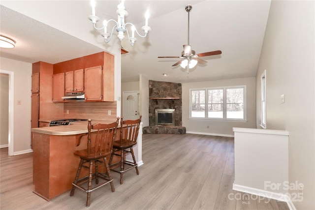 kitchen featuring a breakfast bar, light countertops, open floor plan, under cabinet range hood, and a peninsula