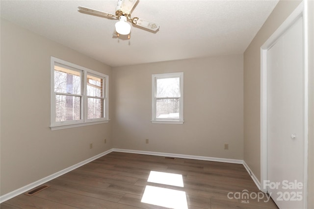 unfurnished room with visible vents, dark wood finished floors, baseboards, and ceiling fan